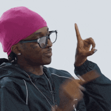a man wearing a pink hat and glasses is pointing upwards