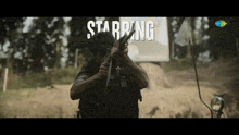 a man holding a gun with the word starring behind him