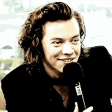 harry styles is holding a microphone in his hand and smiling .