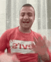 a man in a red shirt is making a funny face and waving at the camera .