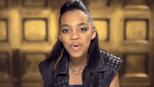 a girl wearing a leather vest and a necklace looks at the camera