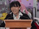 a woman stands behind a wooden podium with a microphone and says sheep on the bottom