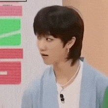 a young man with a mullet hairstyle is wearing a blue cardigan and a white t-shirt .