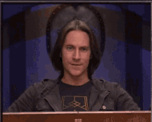 a man with long hair is sitting in front of a wooden box and smiling .