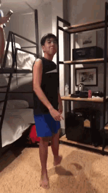 a man in a black nike tank top and blue shorts is dancing in a room with bunk beds