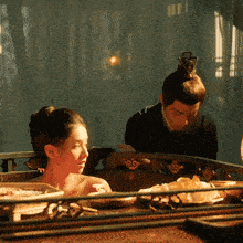 a man and a woman are sitting in a room and the woman is wearing a bun