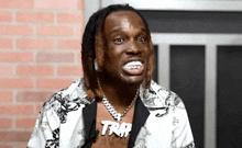 a man with dreadlocks and a necklace that says trap is making a funny face .