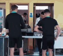 two men are standing in a kitchen with a sign on the wall that says ' no smoking '