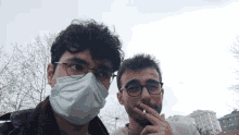 a man wearing glasses and a mask stands next to another man