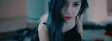 a woman with long blue hair and red lips is kneeling down and looking at the camera .
