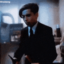 a young man in a suit and tie is standing in a room holding a knife .