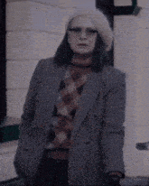 a woman wearing a plaid sweater and a beret stands in front of a building