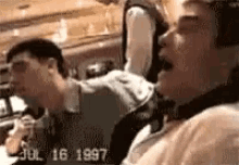 two men are sitting in a car with the date july 16 1997 on the bottom right corner .