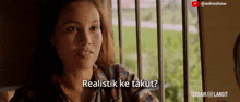 a woman sitting in front of a window with the words realistik ke takut written below her