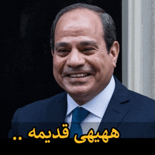 a man in a suit and tie is smiling in front of a sign with arabic writing on it