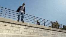 a man is jumping over a fence while another man sits on a wall
