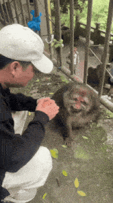 a man in a white hat is petting a monkey on the ground