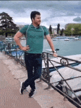 a man in a green shirt is leaning on a railing overlooking a body of water .