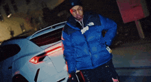a man wearing a blue north face jacket stands next to a white car