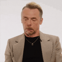 a man with a beard wearing a jacket and a necklace looks down