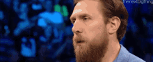 a man with a beard is standing in front of a blue background and looking at the camera .