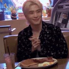 a young man is sitting at a table with a plate of food and a drink .