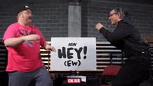 two men standing in front of a sign that says hey