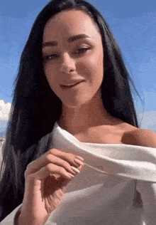 a woman with long black hair is wearing a white off the shoulder top and smiling .