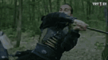a man in armor is holding a sword and another man is holding a sword in the woods .