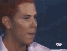 a man with red hair and a white shirt is looking at the camera .