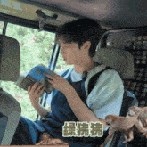 a man sits in the back seat of a car reading a book with chinese writing on it