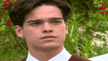 a close up of a man 's face with a white shirt and brown jacket