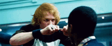 a man with red hair is holding a knife in his hand and fighting another man .