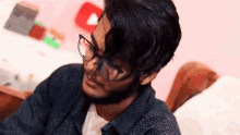 a man with glasses and a beard is sitting on a bed and making a funny face .