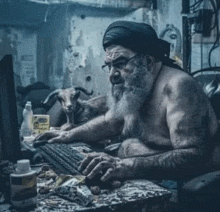 a shirtless man with a beard is typing on a computer keyboard while a goat watches .