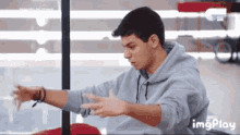 a young man in a grey hoodie is stretching his arms .