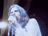 a man with long blue hair singing into a microphone while wearing a white shirt