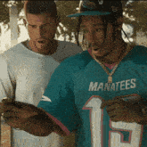 a man wearing a blue manatees jersey looks at his phone