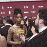 a woman in a gold dress is being interviewed by a man wearing a yellow microphone that says playbill