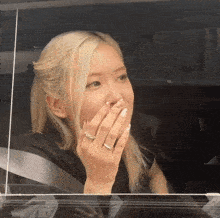 a woman with blonde hair and a ring on her finger looks out a car window
