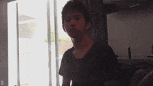 a man in a black shirt stands in front of a sliding glass door with the letter d visible in the corner