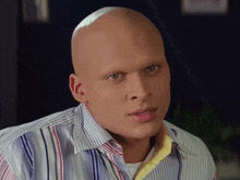 a bald man with no eyebrows is wearing a striped shirt and making a funny face .