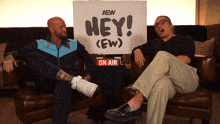 two men sit on a couch in front of a sign that says " hey "