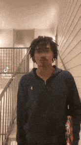 a man with dreadlocks and glasses is standing in front of a staircase with a tiktok icon on the bottom right