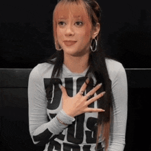 a woman wearing a shirt that says " duh " on it holds her hand to her chest