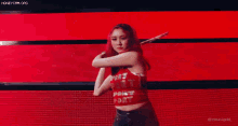 a woman in a red crop top is dancing on a stage with a light coming out of her hand .