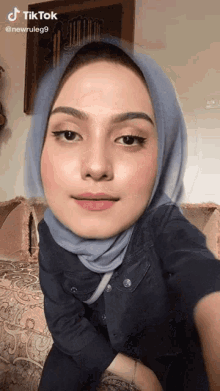 a woman wearing a hijab is sitting on a couch and has a tiktok watermark on her face