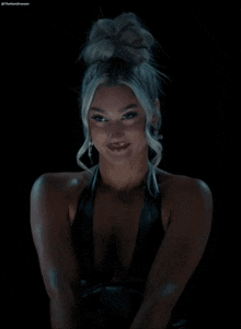 a woman in a black dress with a bun in her hair is looking at the camera