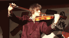 a man in a red jacket is playing a violin in front of chinese writing