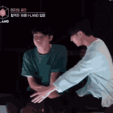 two men are sitting next to each other and one is touching the other 's hand .